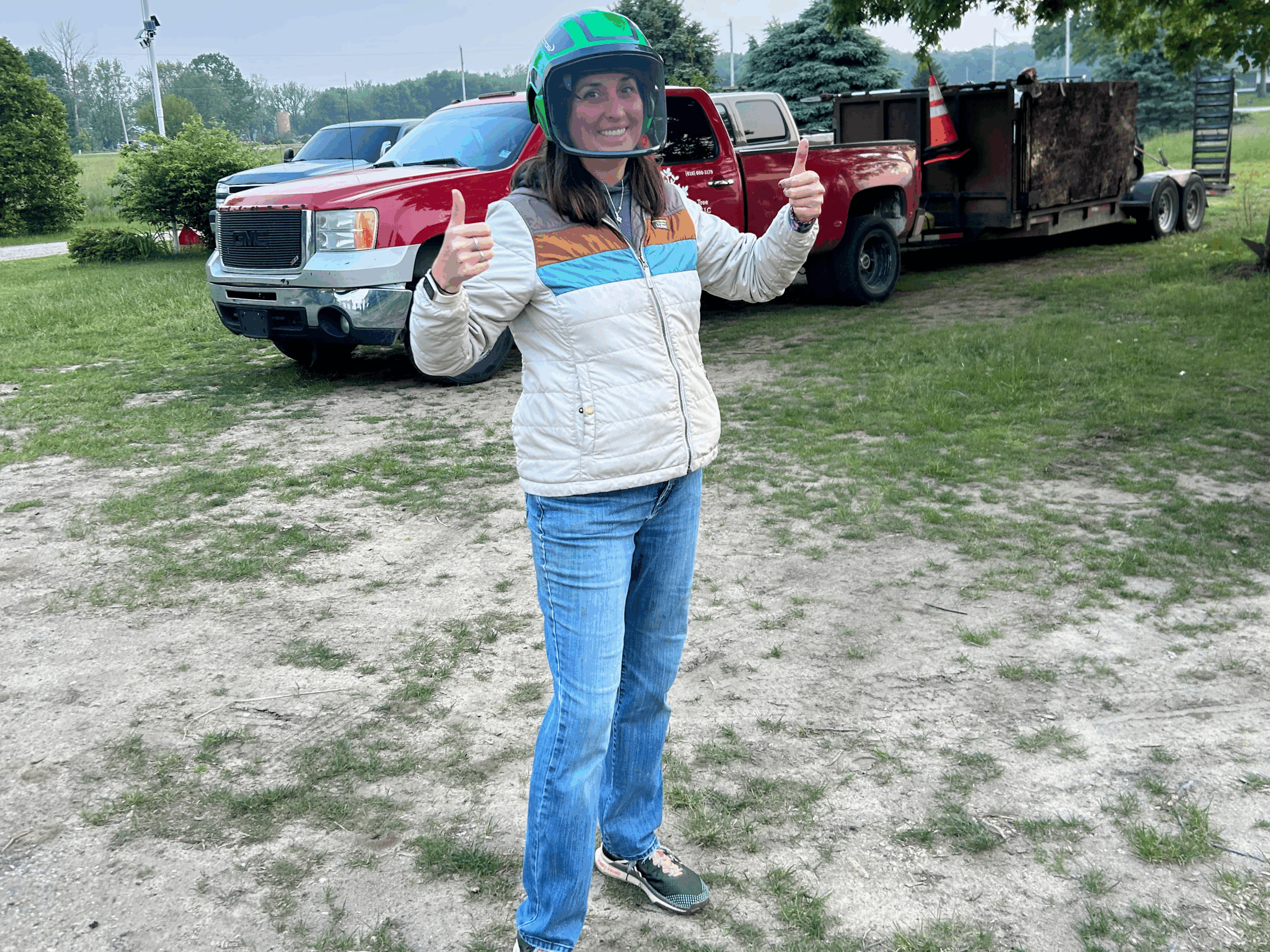 A woman wearing a green helmet and a jacket gives a thumbs-up